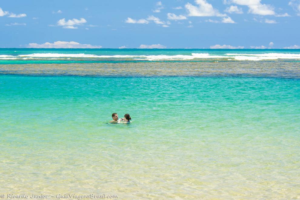 Imagem de um casal juntinhos no mar azul encantador da Praia de Taipu de Fora.